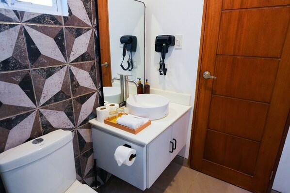 Un baño con lavamanos blanco, espejo, inodoro y un mueble con artículos de aseo.