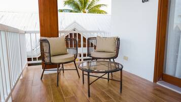 A balcony with two wicker chairs and a glass table, white railing, and a palm tree view.
