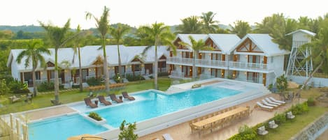 A resort with a large swimming pool, multiple lounge areas, and a well-maintained garden.