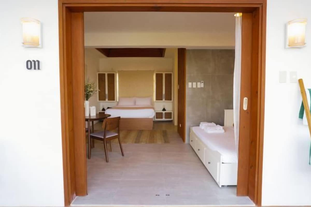 A hotel room with a bed, a desk, and a chair. There are cabinets and a small table with a plant.