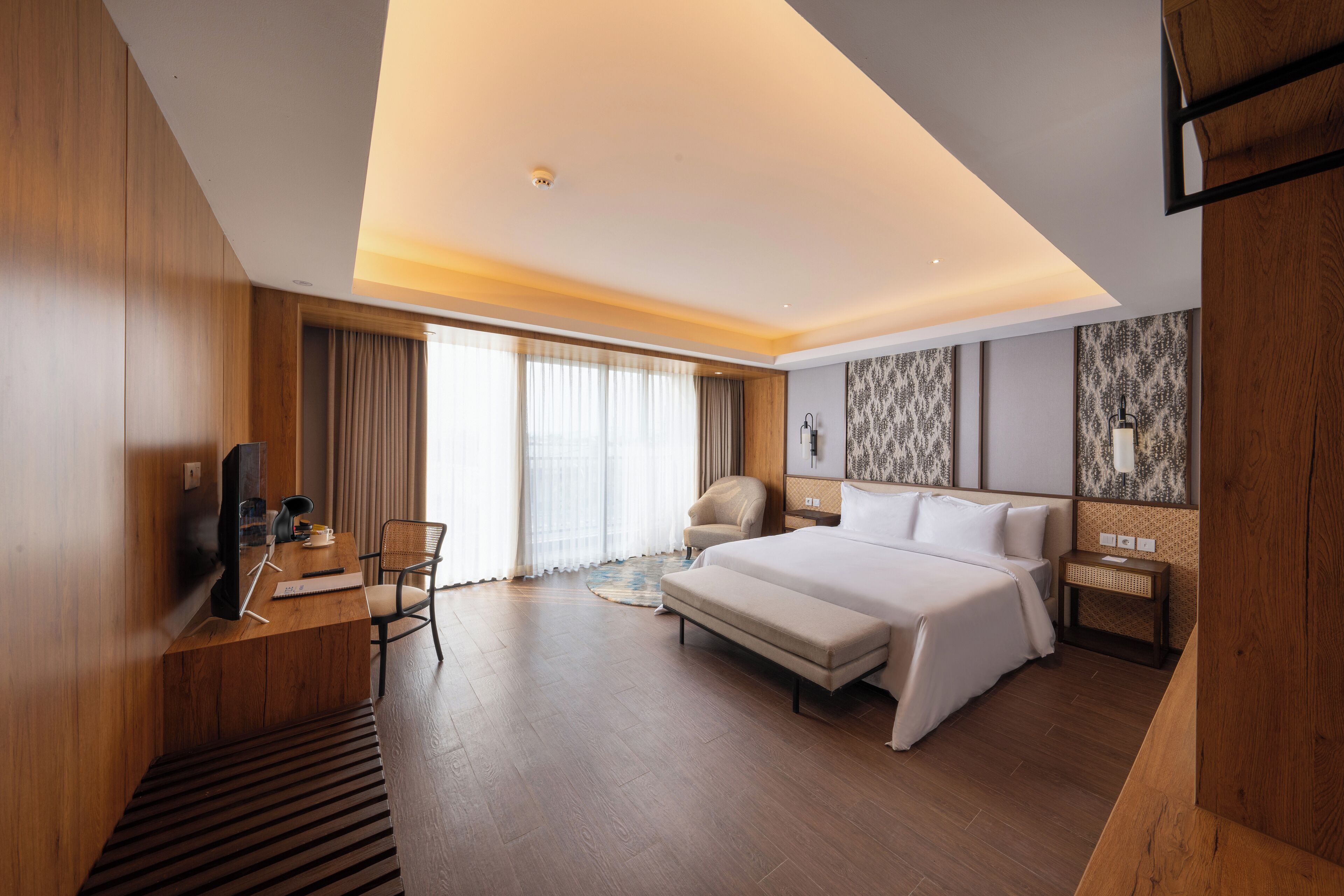 A modern hotel room with a large bed, a desk with a computer, a chair, and a television.
