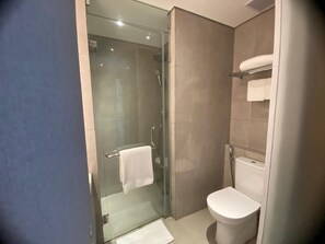 A modern bathroom with a glass-enclosed shower, a toilet, and a towel rack. - Myze Hotel Sumenep (Sumenep)