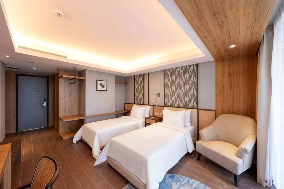 A hotel room with two beds, a chair, a desk, and a small table.