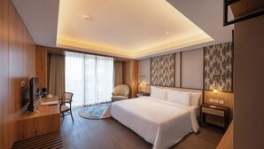 Una habitación de hotel moderna con una cama grande, un escritorio con una silla, un televisor y una pequeña mesa con una lámpara.