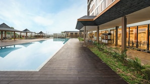 Un hotel moderno con piscina, zona de estar al aire libre y un espacio cubierto con mesas y sillas.
