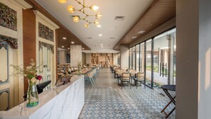 Un moderno vestíbulo de hotel con mostrador de recepción de mármol, suelo con diseño y una amplia zona de comedor con mesas y sillas.
