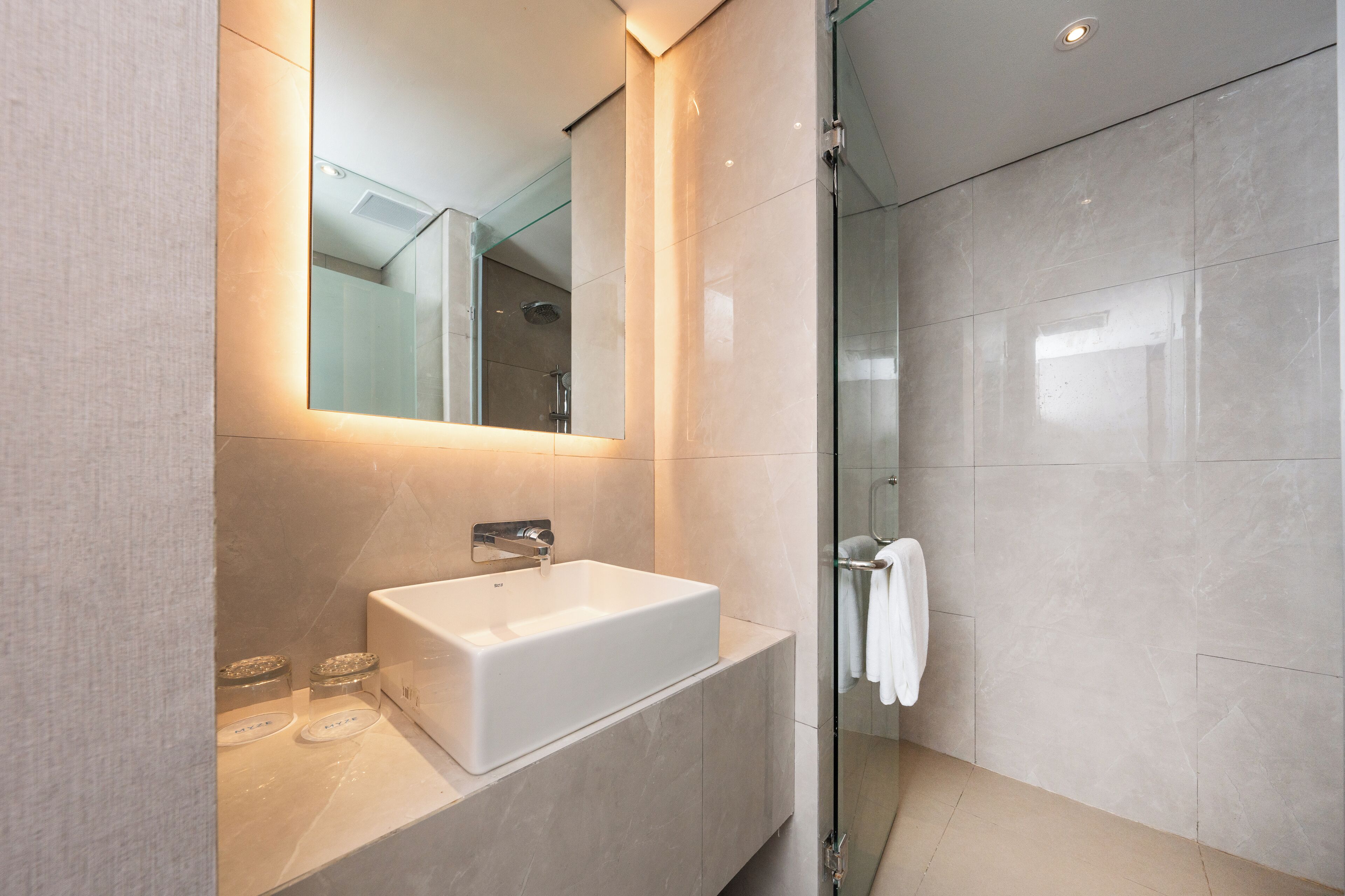 A modern bathroom with a large mirror, a white sink, and a glass shower enclosure.