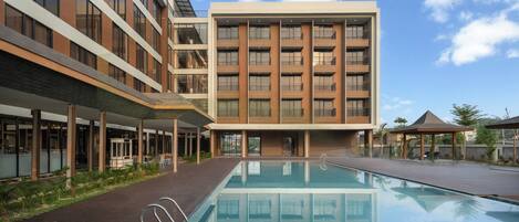A modern hotel with a swimming pool, multiple floors, and a covered outdoor area.