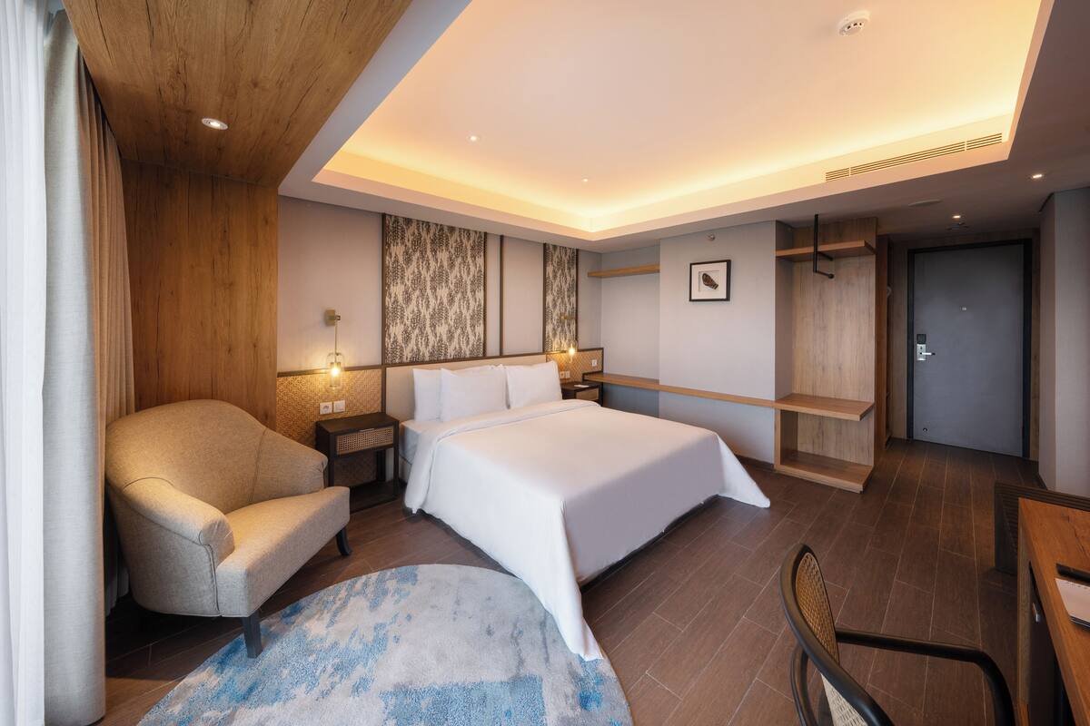 A modern hotel room with a large bed, a sofa, a desk, and a walk-in closet.