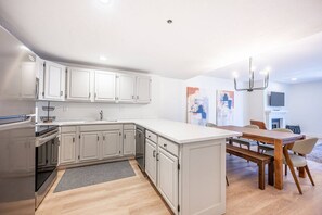 A modern kitchen with white cabinetry, a central island, and a dining area with a wooden table and chairs.