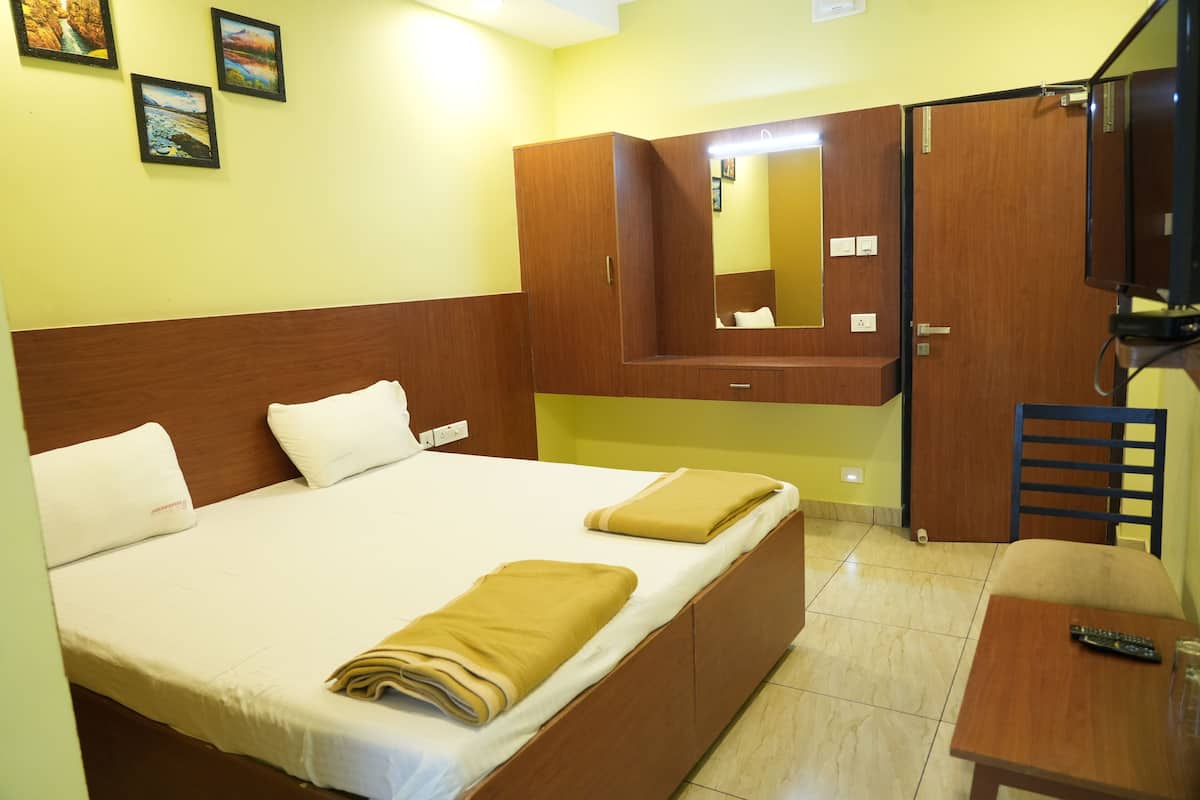 Habitación de hotel con cama, armario de madera, espejo, televisor y una mesita con control remoto.