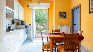 A modern kitchen with white cabinets, a microwave, and a dining area with a wooden table and chairs. - Arancia by Interhome (Imperia)
