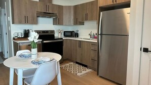 Una cocina moderna con armarios de madera, un refrigerador de acero inoxidable, un microondas y una estufa. Hay una mesa de comedor con sillas y un florero con flores.