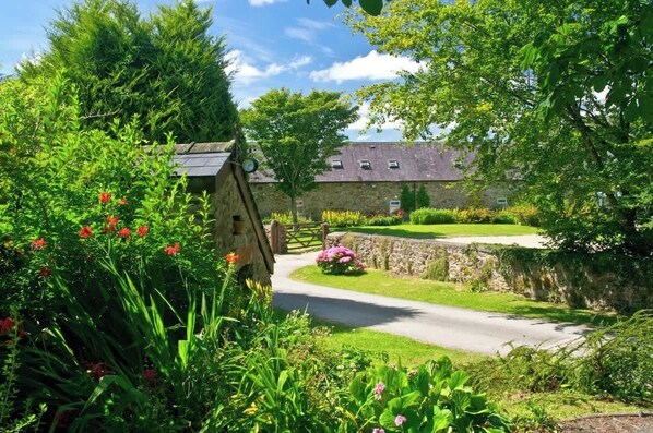 A rural setting with a stone building, a winding road, and lush greenery.