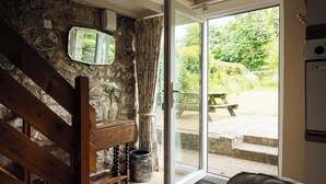 Een rustiek interieur met een stenen muur, een houten trap en een schuifdeur naar een buitenruimte met een bankje en treden.