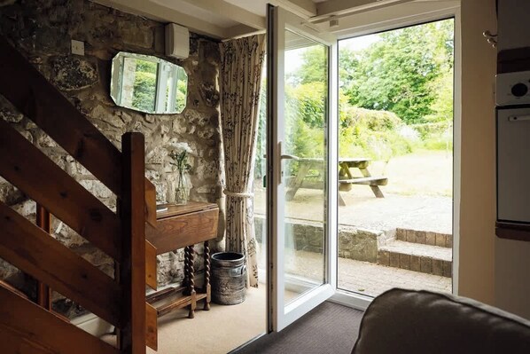 A rustic interior with a stone wall, wooden staircase, and a sliding glass door leading to an outdoor area with a bench and steps.