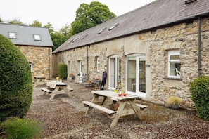 A stone building with a gravel courtyard, wooden picnic tables, and a bicycle.