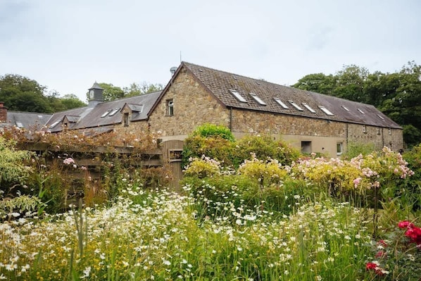 A stone building with a sloped roof and skylights, surrounded by a garden with various flowers.