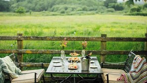 Een buitenterras met een tafel, stoelen en uitzicht op een groen veld.