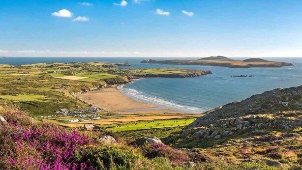 Un paisaje costero con una playa, colinas onduladas y cielo despejado.