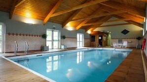 Una piscina interior con vigas de madera, suelo de baldosas y agua de color azul cristalino.