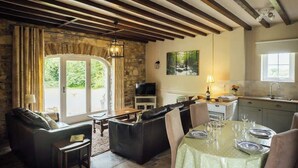 Una sala de estar acogedora con chimenea de piedra, un comedor con mesa dispuesta para cuatro, y una cocina con ventana.