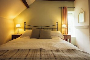 Un lit avec une tête de lit, deux tables de chevet avec des lampes, une fenêtre avec des rideaux et un miroir au mur.