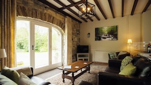 Una sala de estar con pared de piedra, techo de madera, televisor, chimenea, sofá, mesa de centro y un cuadro en la pared.