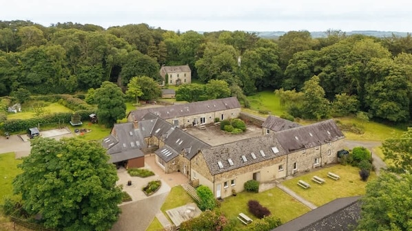 Un grand bâtiment en pierre, doté de nombreuses pièces et d’une cour, entouré d’une végétation luxuriante.