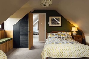 A bedroom with a sloped ceiling, a bed with a patterned bedspread, a bedside table with a lamp, and a framed picture on the wall.