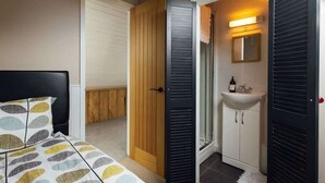 Ein Schlafzimmer mit einem Bett, einer Holztür, einem Badezimmer mit Waschbecken und Spiegel sowie einem weißen Schrank.