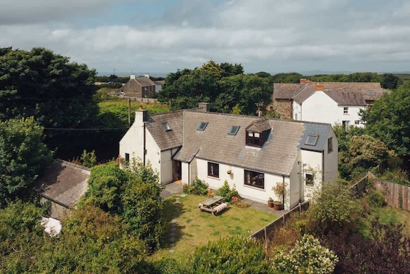 A white house with a sloped roof, a small garden, and a wooden bench.