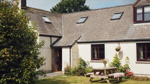 Ein Haus mit geneigtem Dach, einer Veranda und einem kleinen Garten mit einer Holzbank.