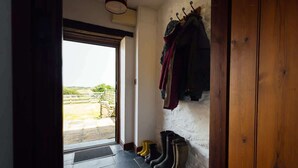 A room with a view through a door, a coat rack with clothes, and several boots against the wall. - Cosy Stone Cottage w/ Log Burner & Views (Nolton)