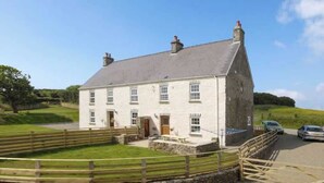 A white stone house with a steeply pitched roof, a wooden fence, and a paved driveway. - Cosy Stone Cottage w/ Log Burner & Views (Nolton)