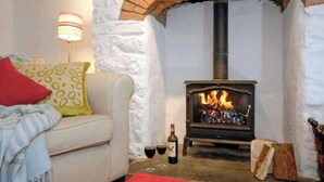 A cozy living room with a fireplace, a sofa, a lamp, and a bottle of wine. - Cosy Stone Cottage w/ Log Burner & Views (Nolton)