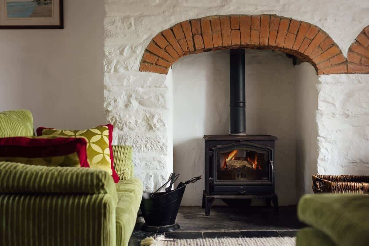 A cozy living room with a brick fireplace, green upholstered furniture, and a rustic white wall.