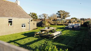 A house with a grassy yard, a wooden table, and a small shed.