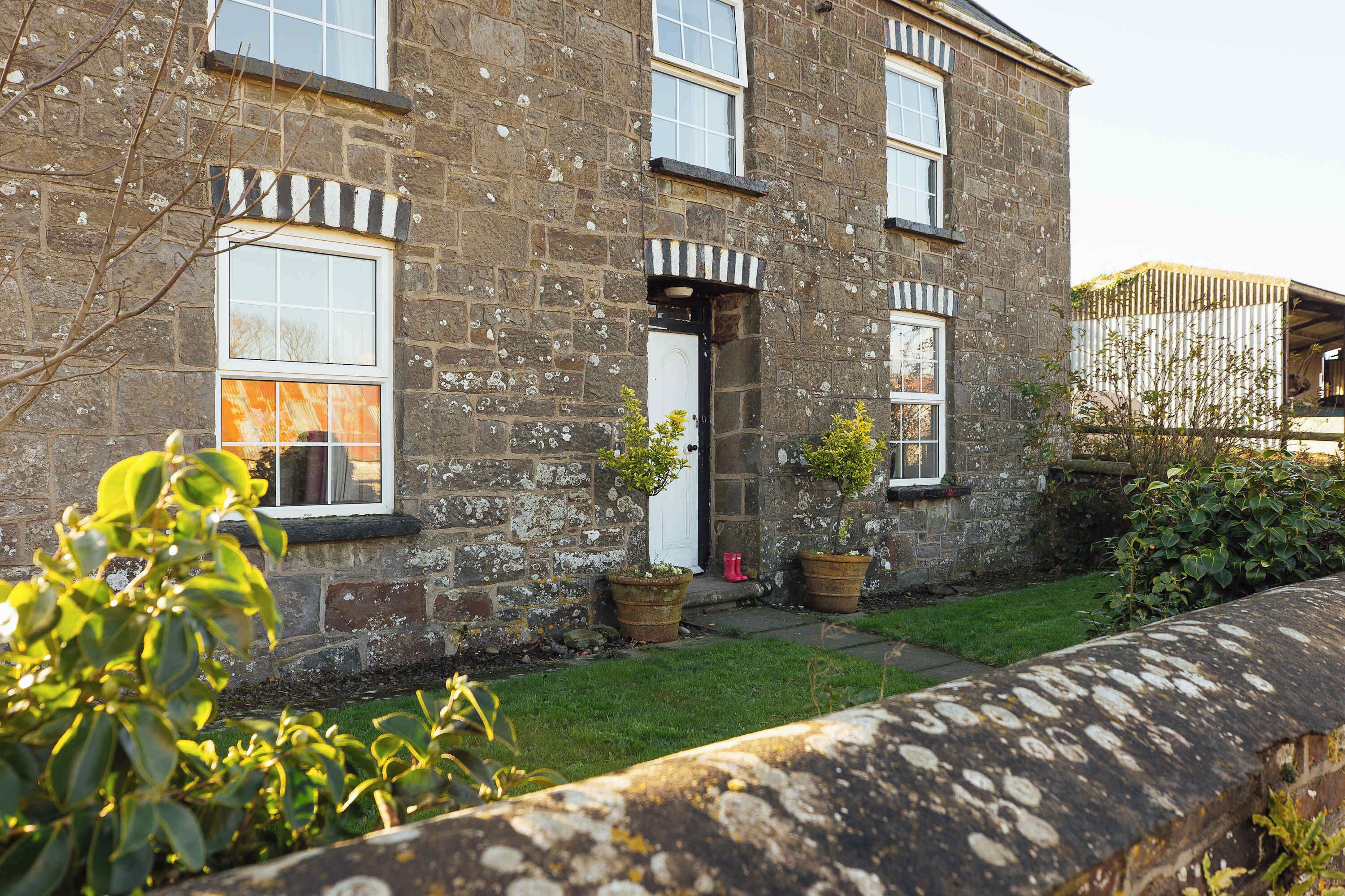 A stone building with multiple windows, a door, and potted plants in the yard.