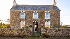 A stone building with a central entrance, multiple windows, and a gravel driveway.