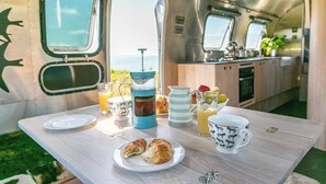 A kitchen area with a table set for breakfast, including croissants, a coffee pot, and a pitcher of juice. - Airstream with Stunning Coastal Views. (Nolton Haven)