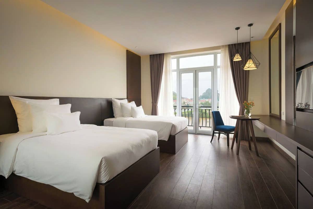 Een hotelkamer met twee bedden, een kleine tafel met stoel, een balkon met uitzicht en een televisie.