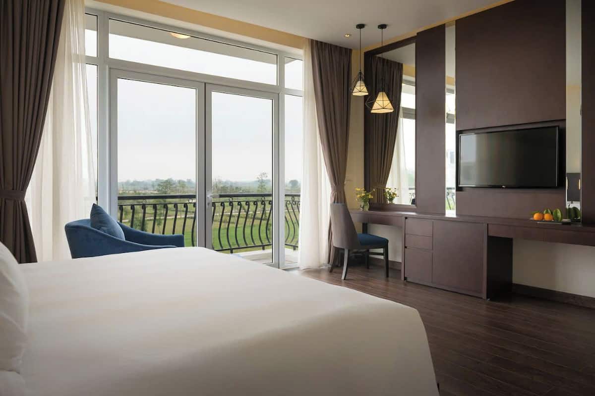 Een hotelkamer met een groot bed, een bureau met een stoel, een televisie en een balkon met uitzicht op het landschap.