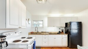 Une cuisine avec des meubles blancs, un réfrigérateur noir, une cuisinière et une machine à café.