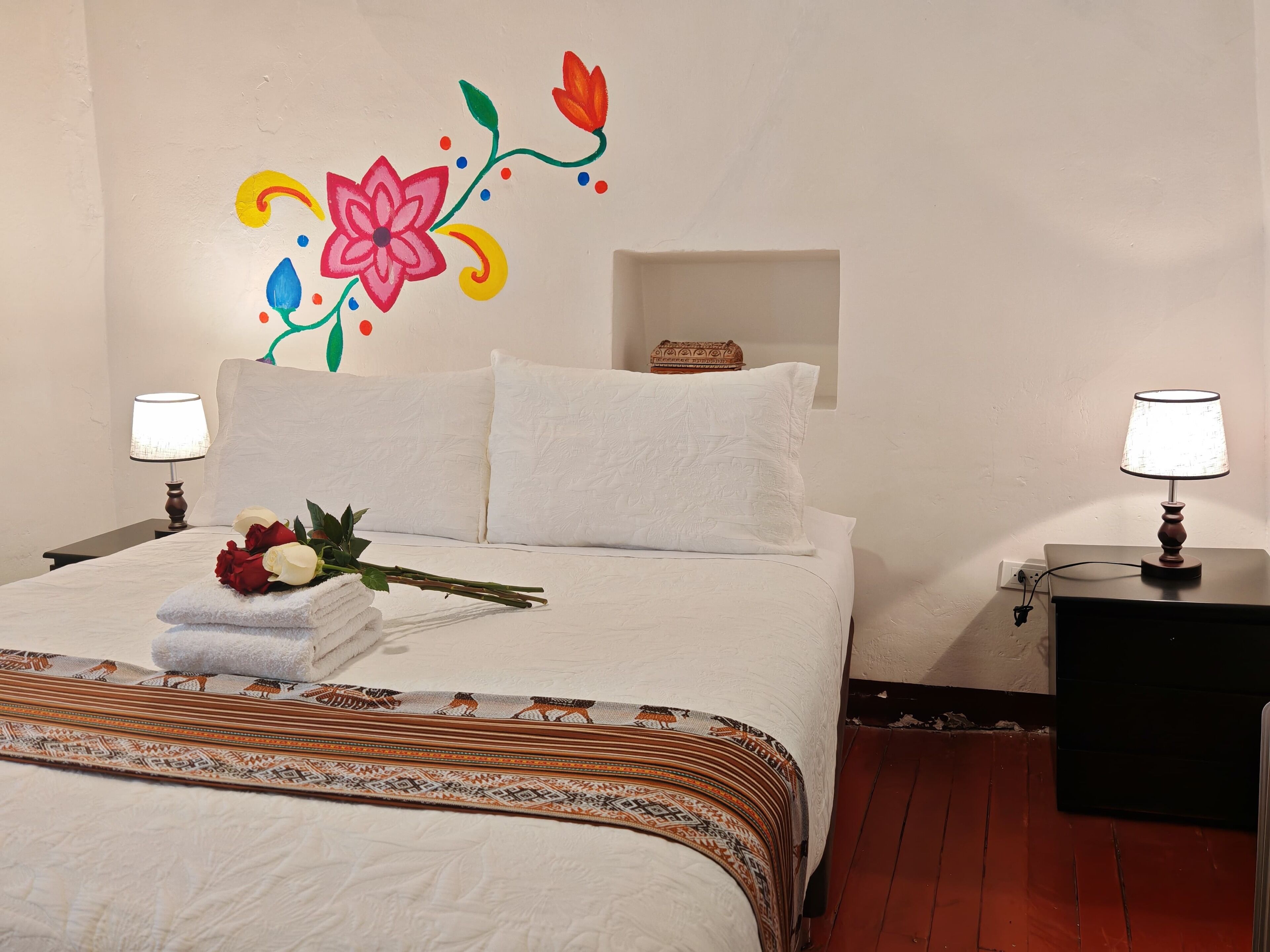 A neatly made bed with white linens, a floral wall decoration, and a bedside table with a lamp.