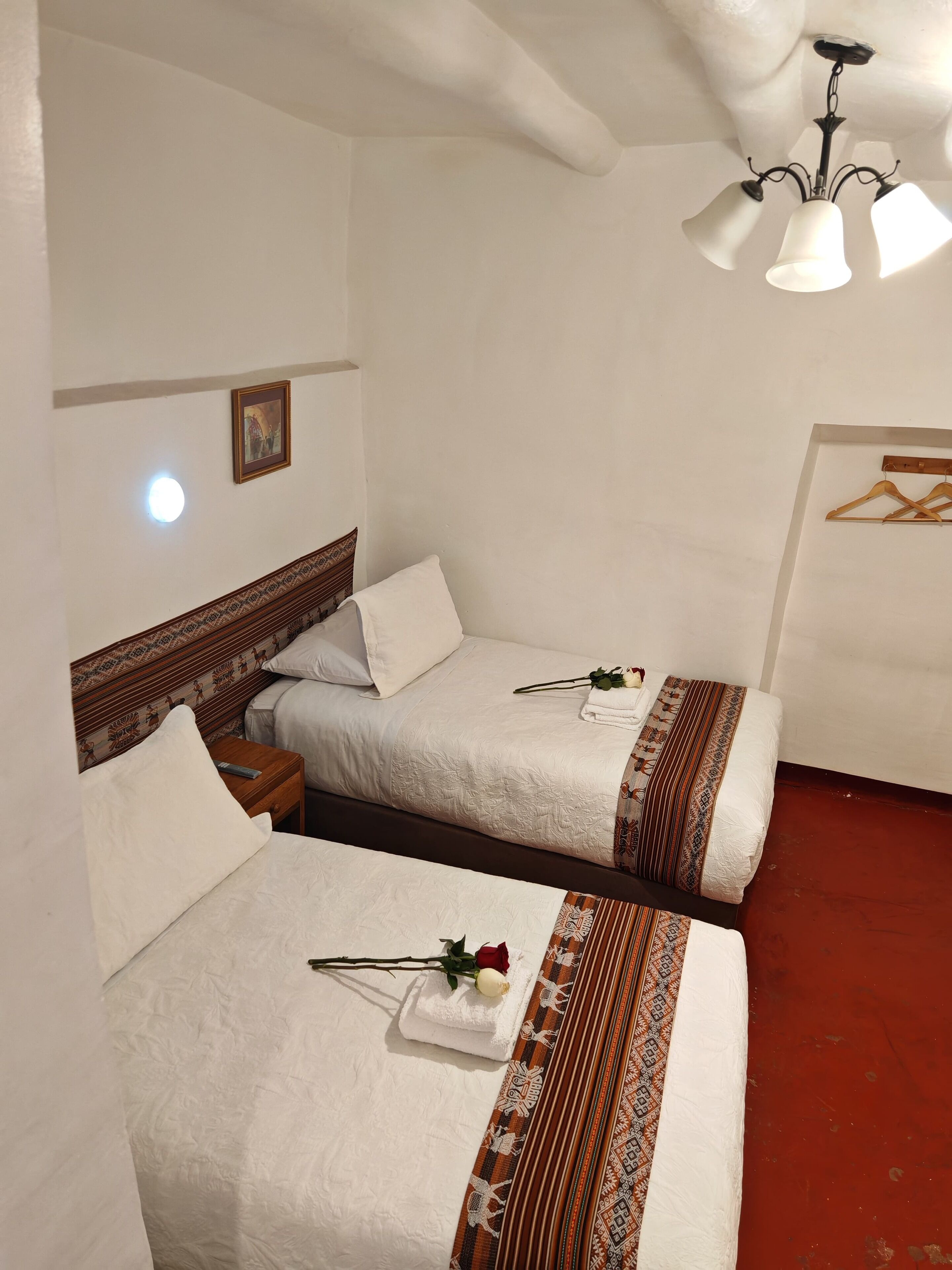 A hotel room with two beds, a wooden headboard, a nightstand, a wall-mounted picture, and a ceiling light fixture.