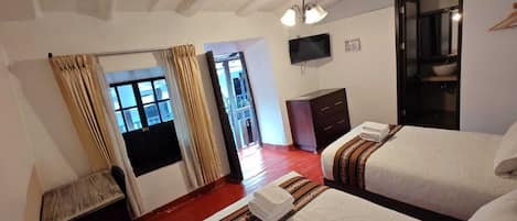 A hotel room with two beds, a TV, a wardrobe, and a bathroom visible through an open door.