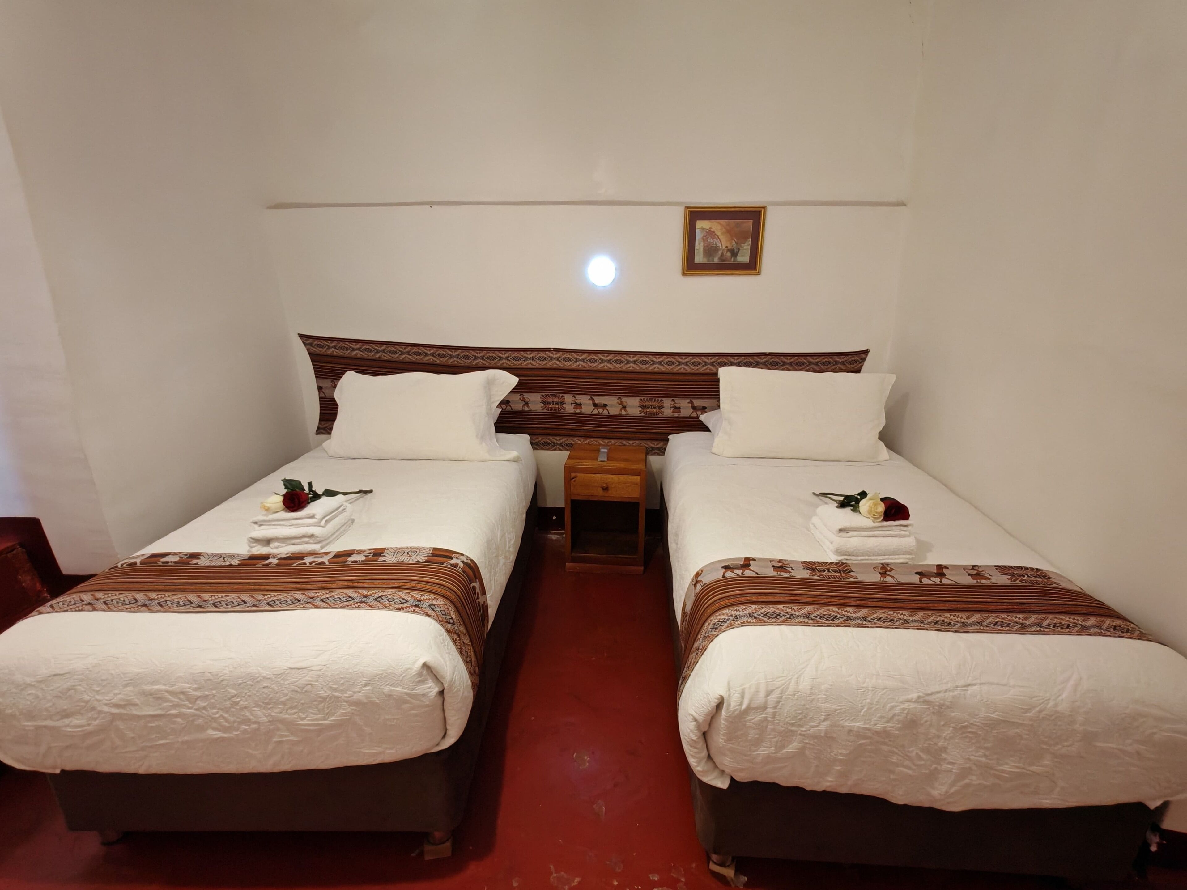 A hotel room with two single beds, each with a patterned headboard, white linens, and a small bedside table with a lamp.