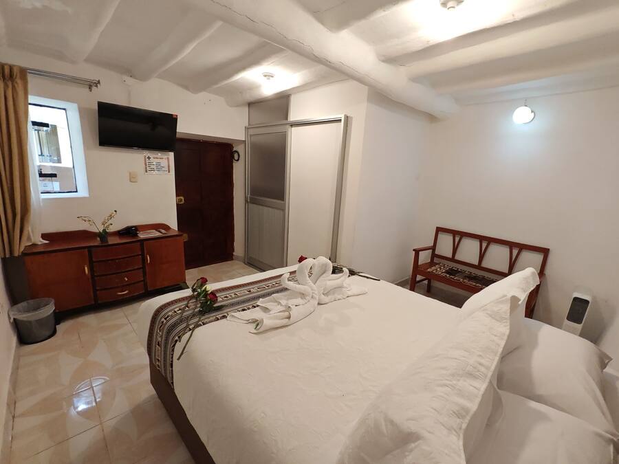 Habitación de hotel con cama, escritorio con teléfono, una silla, televisor montado en la pared y una puerta.
