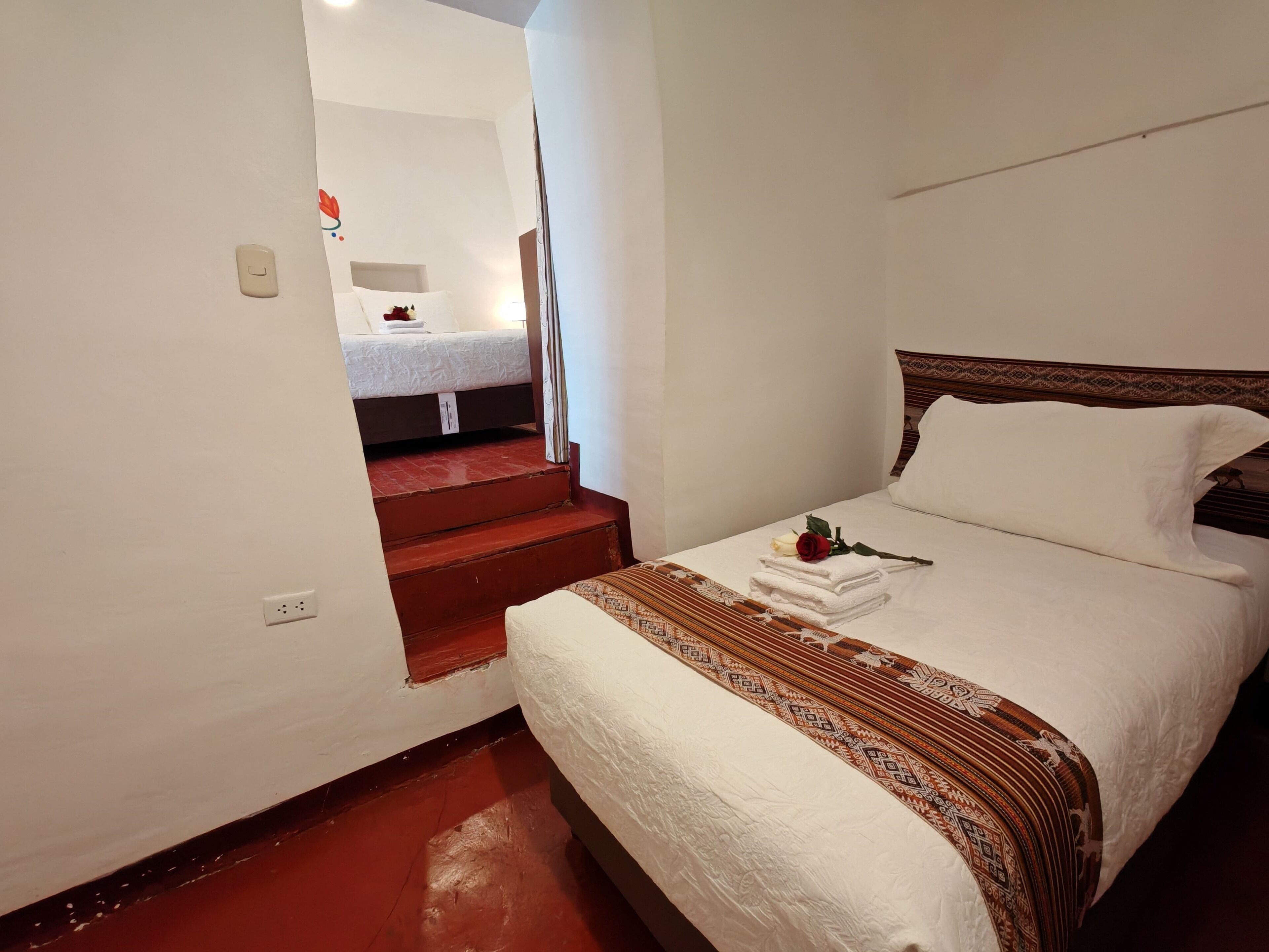 Habitación de hotel con cama, una mesita de noche con lámpara y una escalera que sube a un nivel superior.
